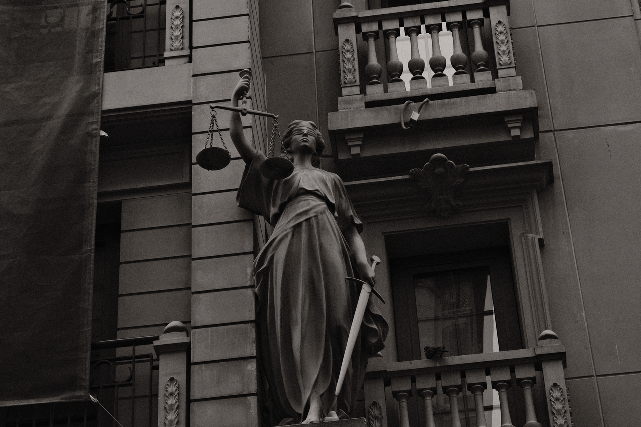 A black and white image of Lady Justice statue against a building facade symbolizing law and fairness.